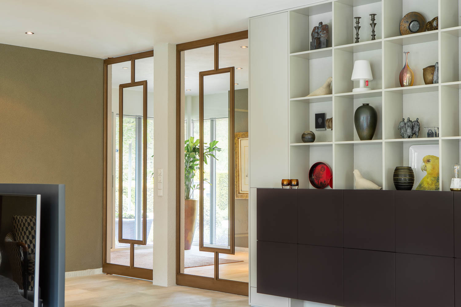 Dubbele bronzen stalen deuren met glas als elegante scheiding tussen hal en woonkamer.